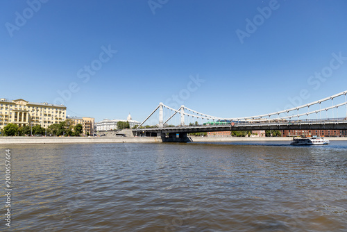 Russia. Moscow. June 06, 2026. Krymsky Bridge suspension structure across the Moskva River with cruise boat on sunny summer day