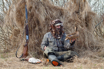 The hunter sits in front of his duck shutter and holds a decoy d