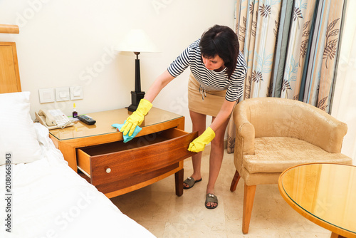 A woman dusts a bedside table under table lamp, a wife's household chores.
