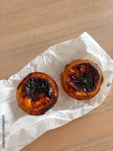 Two traditional Portuguese pastel de nata custard tarts on table, artisanal bakery aesthetic
