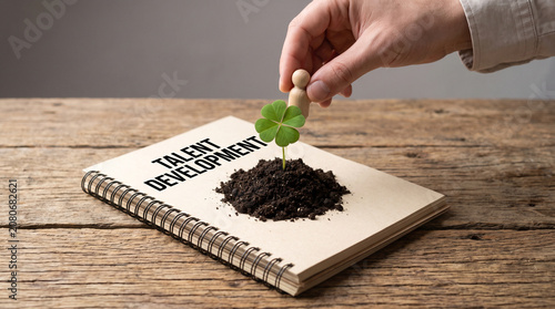 Hand placing wooden figurine near green clover growing from soil on a talent development notebook