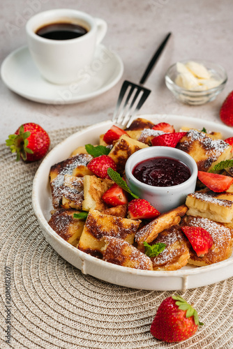 Traditional Austrian Kaiserschmarrn shredded pancake served with fresh strawberries, powdered sugar, and berry jam fruit sauce on a plate