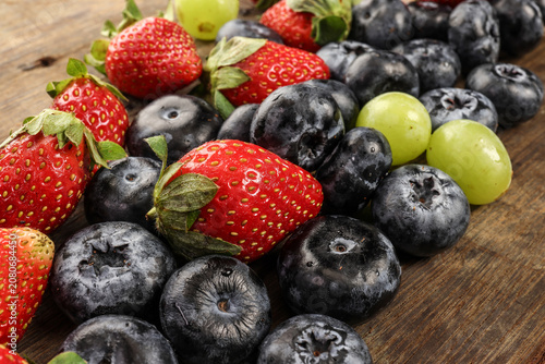 Fresh ripe Blueberry strawberry grape macro closeup on wood dark white background
