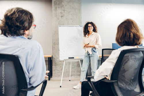 Smiling woman with curly hairstyle and eyeglasses presenting business strategy at office meeting