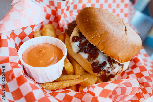 Juicy burger with crispy french fries and dipping sauce in red checkered basket