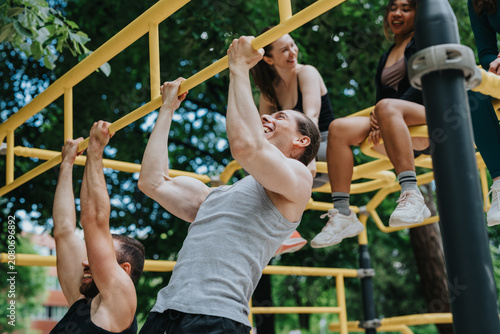 Obraz na plátně A group of young friends perform pull-ups and hang from yellow outdoor bars while smiling and training