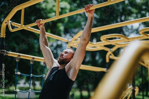 Canvas Print A fit bearded man performs a pull up on yellow monkey bars