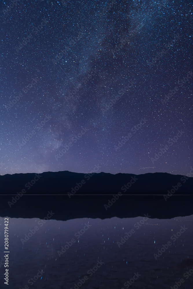 Fototapeta premium Sierra Nevada mountain silhouette under starry night sky with Milky Way reflection on calm water
