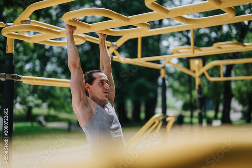 Photography A man performs an upper-body exercise while hanging from yellow monkey bars