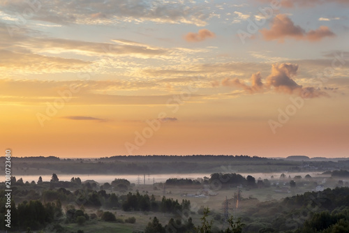 The bright, shining sky at sunrise and the creeping fog above the outlined silhouette of the horizon