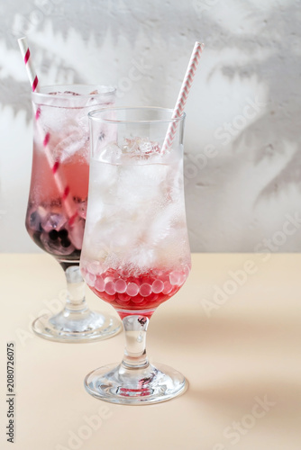 Two glasses of lemonade with ice, tapioca balls and berry syrup