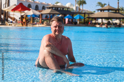 Happy overweight man sitting water shallow pool.