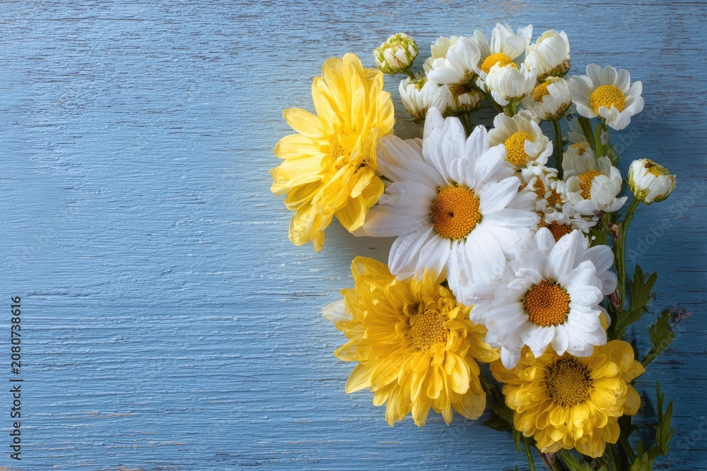 Obraz premium A vibrant bouquet of daisies and yellow blooms rests on a textured, faded blue wooden surface