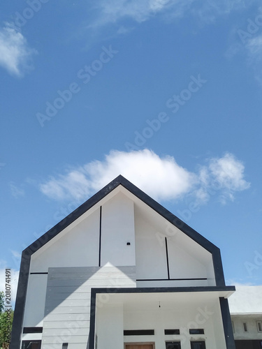 A minimalist modern house roof with clean lines and black trim, captured from a low angle under a bright blue sky with scattered white clouds