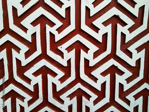 Detailed view of a wall featuring a repeating geometric pattern in contrasting shades of red and white, creating a visually striking and textured surface.
