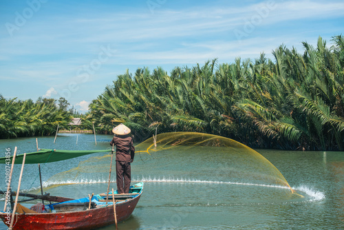 Vietnamese fisherman casting a large yellow net from a traditional wooden boat