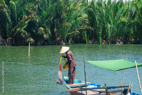 Vietnamese fisherman casting a large yellow net from a traditional wooden boat