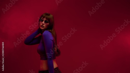 Young woman adjusting sunglasses in red studio wearing blue crop top, long hair, moody fashion light
