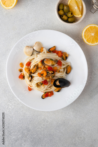 Italian pasta with mussels and tomatoes served on a white ceramic plate, with lemon slices and olives on a bright background