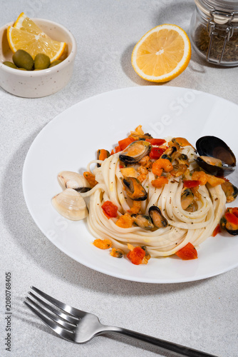 Italian pasta with mussels and tomatoes served on a white ceramic plate, with lemon slices and olives on a bright background