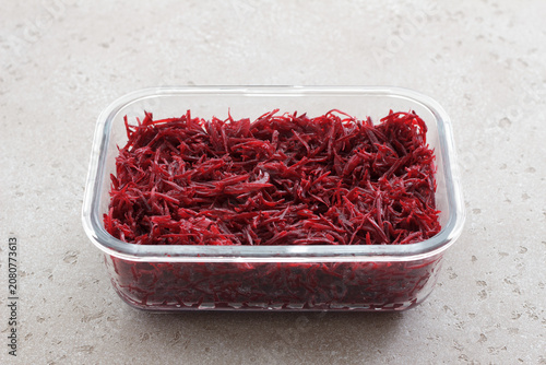 Fresh grated beetroot salad in a glass food container with fork on a light stone surface. Healthy vegetable dish, meal prep ingredient