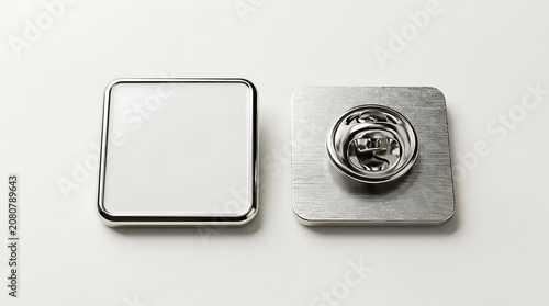 Two square metal badges one blank white face one with pin