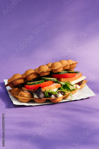 Savory Hong Kong bubble waffle sandwich filled with ham, cheese, fresh tomatoes, cucumbers, and salad greens on a purple background