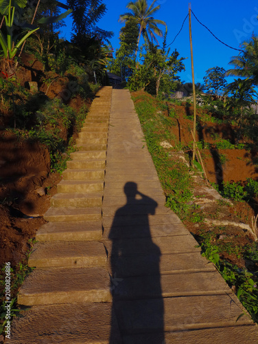 Photography Stone stairs ascend a steep hillside with a human shadow cast prominently upon the path