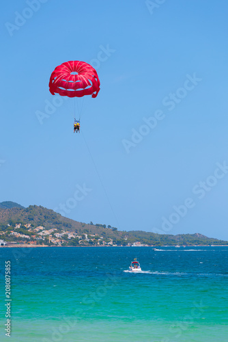 Red parasailing parachute activity over the turquoise sea of Playa de Muro Alcudia Mallorca