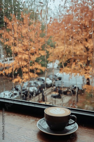 Rain Falls on Window as Coffee Sits on Table, Highlighting Orange Leaves Outs...