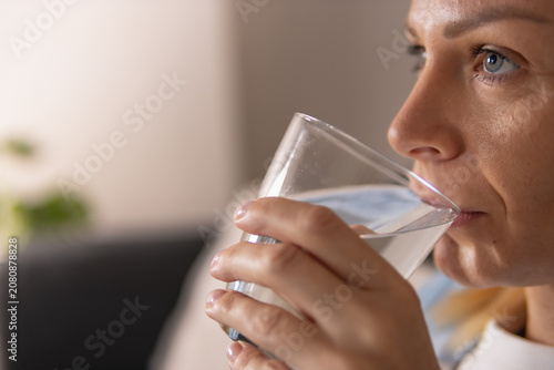 Canvastavla Close up of woman drink water from glass at home, sitting on sofa and taking a refreshing break, showing hydration and healthy lifestyle indoor moment