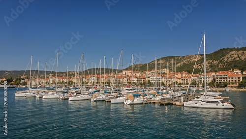 Sailboats Docked in a Harbor With Buildings and Mountains in the Background D...