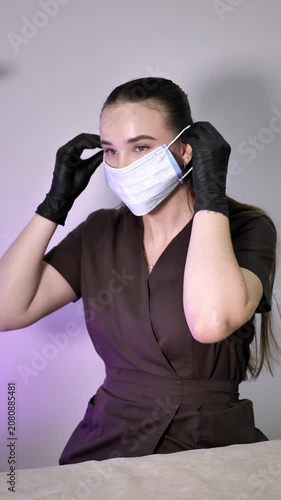 Professional female master in black gloves puts on a protective medical mask at a beauty salon. Vertical medium shot. Concept of safety, hygiene and preparation for cosmetic procedure