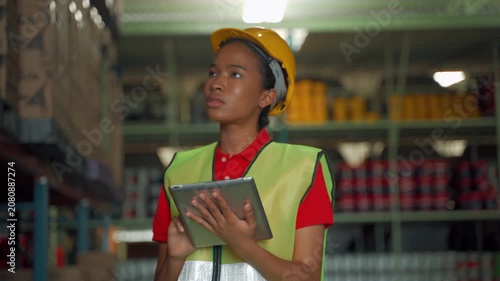 Warehouse employee wearing a safety helmet and reflective vest using a digital tablet to manage inventory inside a distribution warehouse. Smart warehouse technology, logistics, inventory tracking, an