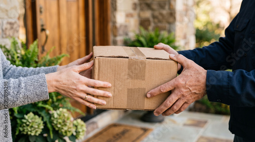 Hands of courier and customer exchanging cardboard delivery box at front door