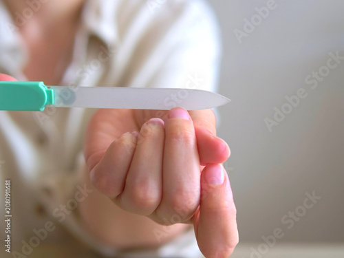woman's hands filing and shaping her fingernails with a glass nail file