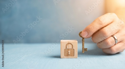 Hand holding a key next to a wooden cube with a padlock icon representing security, privacy, and business solutions