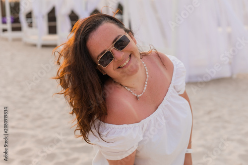 Happy overweight brunette woman wearing sunglasses on the beach at a hotel in summer