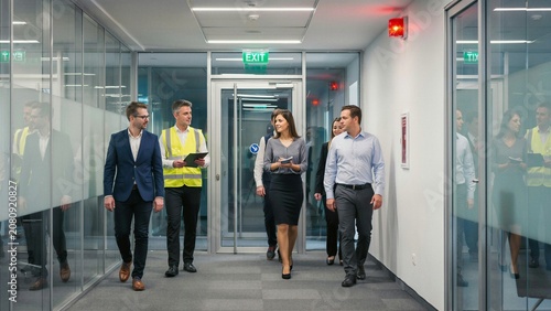 Diverse team of business professionals and a worker walking through a modern glass office hallway engaged in discussion symbolizing collaboration and corporate operations