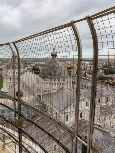 An elevated perspective showcases the intricate architecture of Pisa Cathedral's domes and surrounding urban landscape, partially obscured by a protective metal barrier