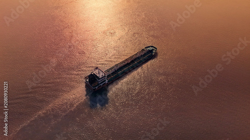 Quadro su tela Cargo Ship Sailing Across Calm Water at Sunset