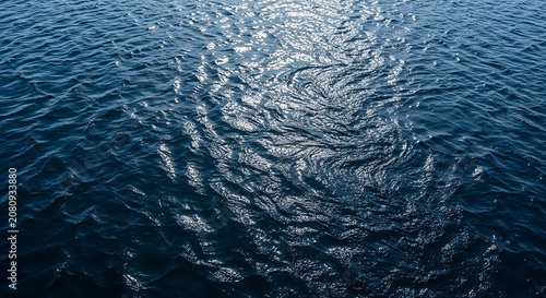 Deep blue ocean water with swirling currents and sunlight glinting on the surface