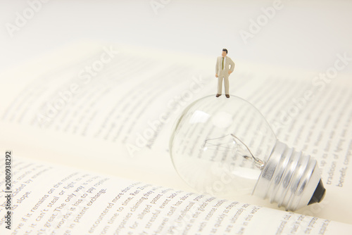 Fotografie Businessman Standing on Light Bulb Over Open Book