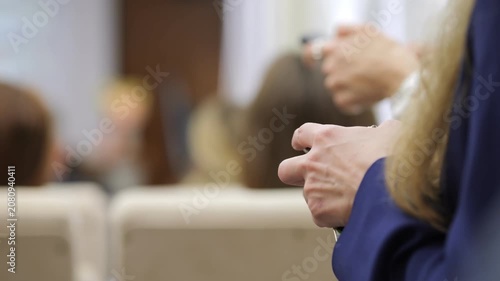 Close-up of hands holding remote controls during a presentation. Audience members focus on speaker. Blurred background shows conference room setting. Suitable for corporate training, business meetings