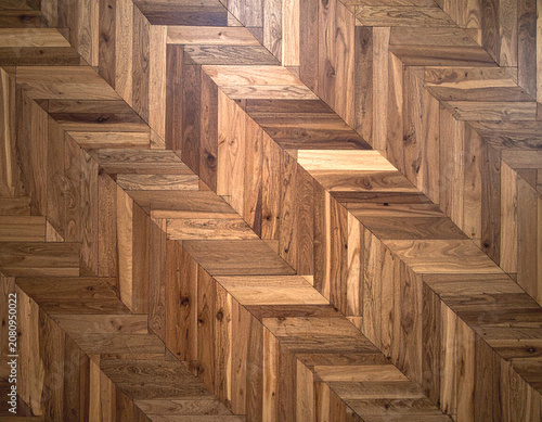A close-up view of an intricately patterned wooden floor with herringbone tiles, showcasing natural wood grain variations and warm brown tones.