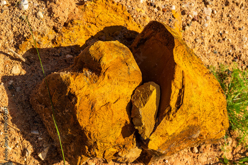 Split limonite rock revealing vibrant yellow ochre pigment, raw geological formation texture found in a dusty open-pit quarry under natural sunlight, detailed mineral background surface