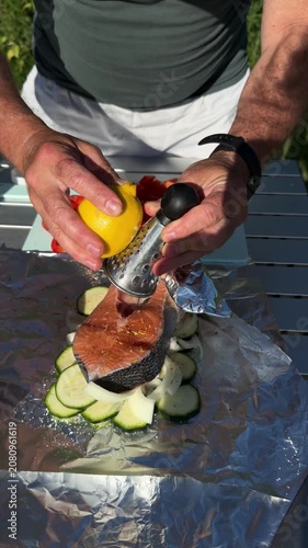 Close up of man grating fresh lemon zest over fish fillet preparing dinner at camp table.