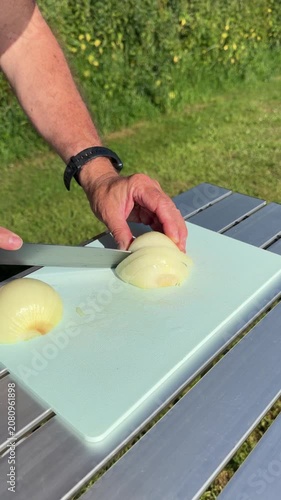 Close up of man hands chopping raw yellow onion on plastic board preparing campsite dinner.