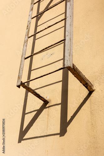 Rusty Metal Fire Escape Ladder Casting Shadow on Beige Wall