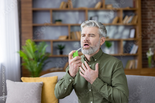 Fotografie Mature man using a throat spray to alleviate discomfort from a sore throat or co